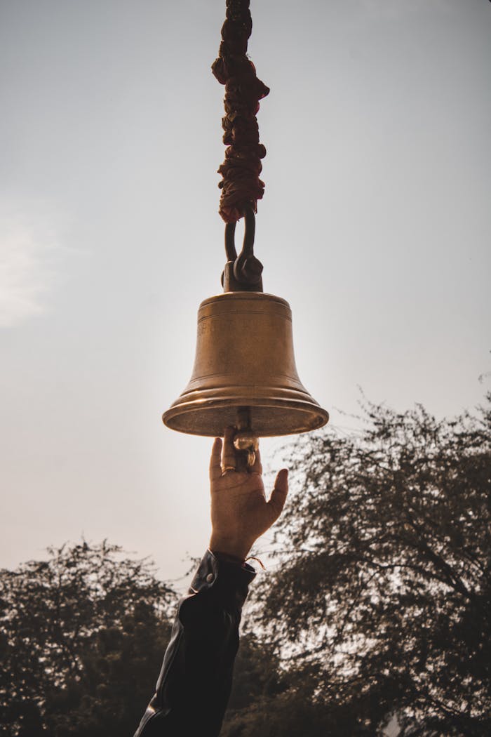 A hand reaches up to ring a bell outdoors in Jaisalmer, Rajasthan, India.