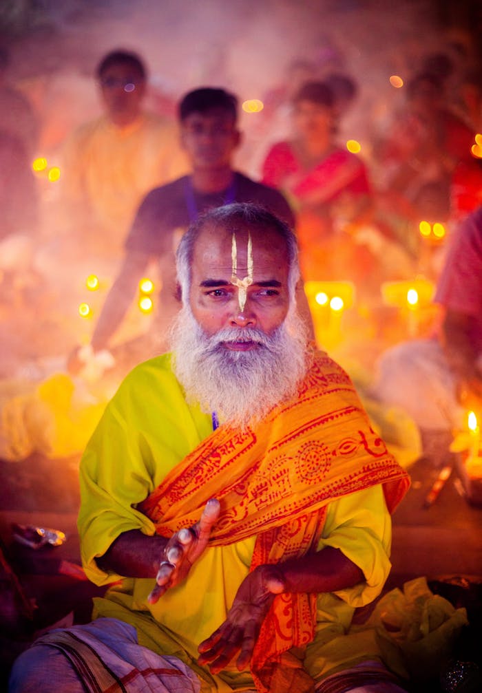 A Hindu priest in vibrant attire performs a ritual surrounded by candlelight, creating a spiritual atmosphere.